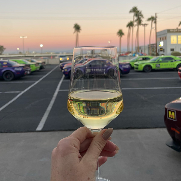 Woman holding a glass of red wine looking at race cars
